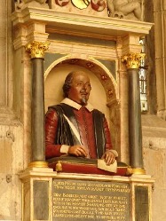 The wall-mounted monument of carved marble shows the upper-half of a balding man with a goatee holding a quill pen in his right hand and a piece of paper or parchment under his left hand.