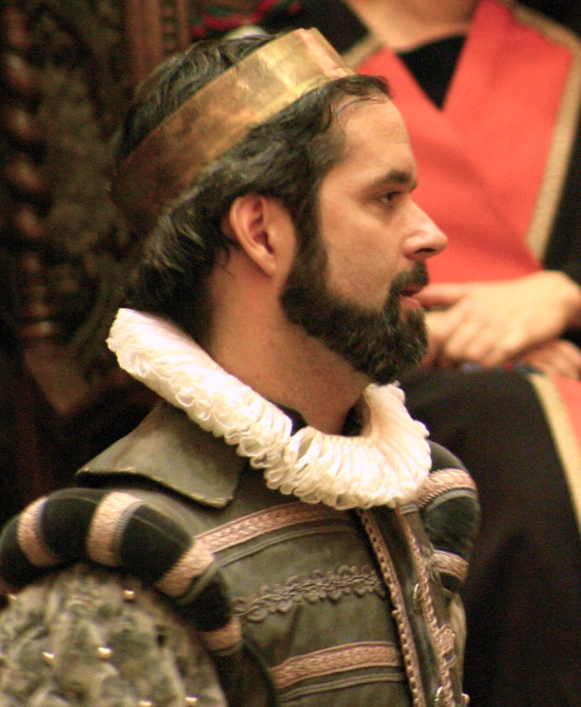 A photo of Scott Clarkson as Cambria. Cambria is a white man with a dark beard wearing a green and gold doublet and a bronze-colour coronet.