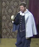 A photo of Paul Hopkins as Gallia. Gallia is a white man wearing a dark blue outfit and silver cape. He is gesturing with one hand.