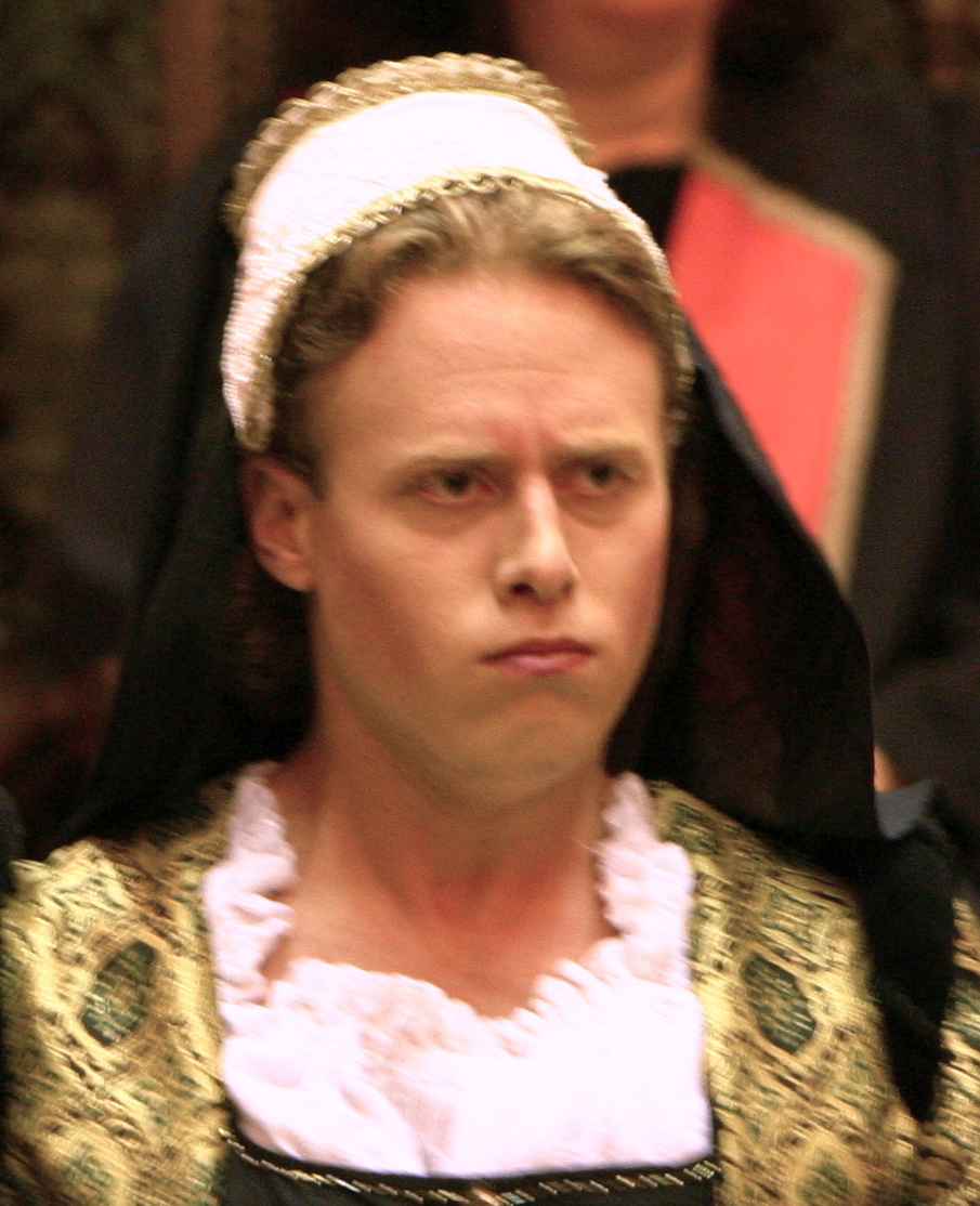 A photo of Gonorill frowning. Gonorill is a white woman wearing clothes with gold detailing.