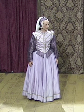 A photo of Derek Genova as Ragan. Ragan is wearing a purple dress and standing with her hands by her side.