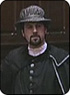 A photo of David Kynaston as Skalliger. Skalliger is a white man with a black goatee and is wearing all black.